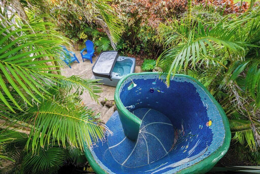 A hot tub surrounded by lush greenery, a blue chair, and a small table.