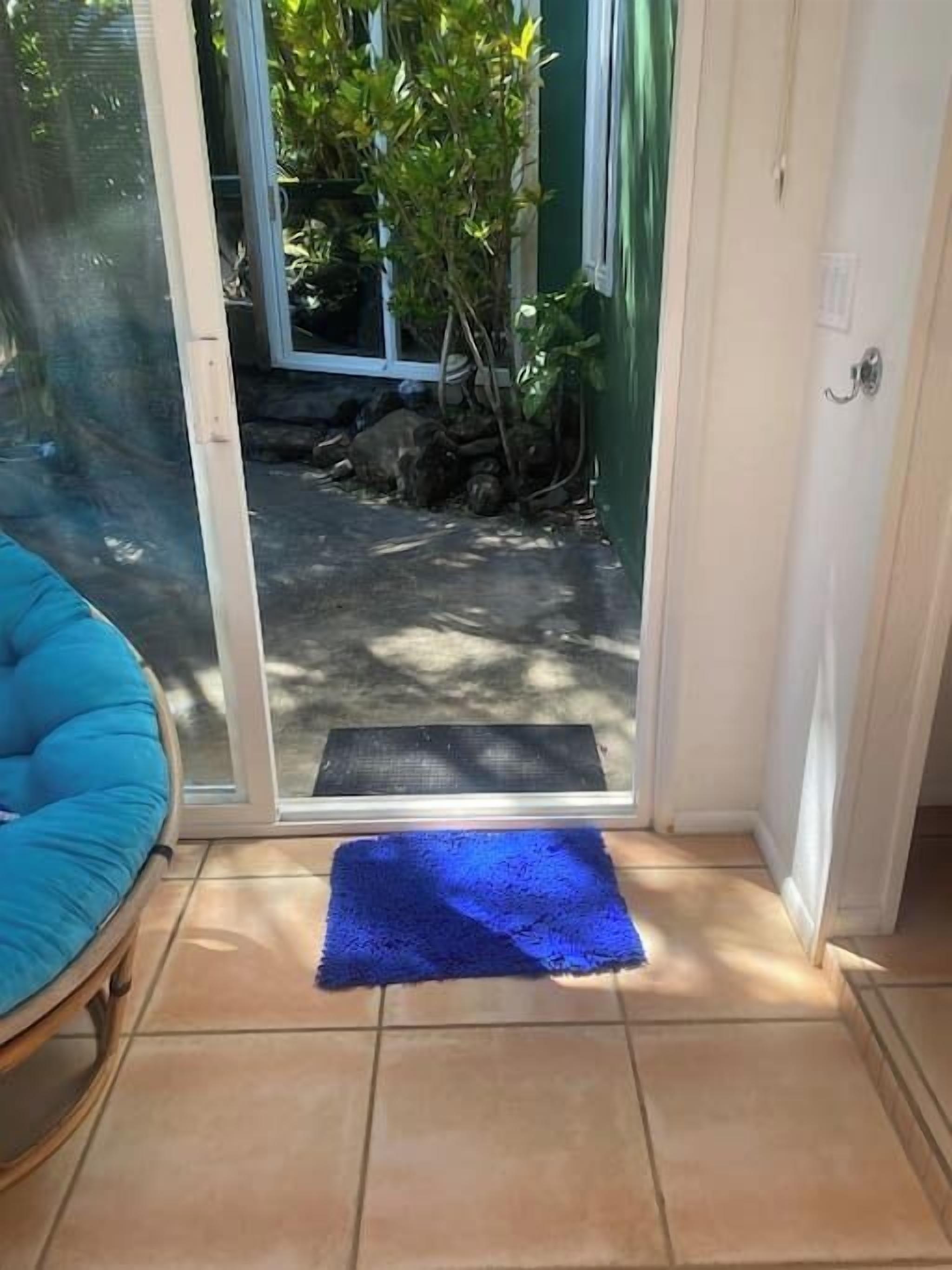 Habitación con puerta de vidrio corrediza que da a un espacio exterior, alfombra azul en el suelo y una silla azul.