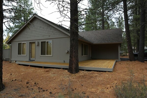 A single-story cabin with a wooden deck, surrounded by trees.