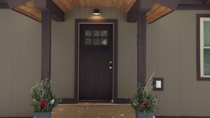 Una casa de madera con una puerta frontal marrón oscuro, un porche cubierto y dos macetas a cada lado de la entrada.