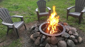 Patio trasero con un pozo de fuego rodeado de rocas y dos sillas Adirondack.