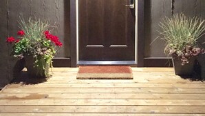 Una puerta de madera con un ventanal encima, flanqueada por dos macetas con flores rojas.