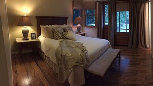 A bedroom with a large bed, two bedside lamps, a bench, a nightstand, and a window with curtains. - Beautiful Lake Whatcom/Sudden Valley House Rental steps from the water (Bellingham)