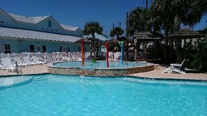 Una piscina con tobogán, sillas de descanso y un edificio al fondo.