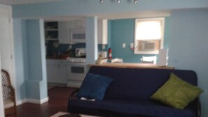 Een woonkamer met een blauwe bank, een houten salontafel en een keuken op de achtergrond.
