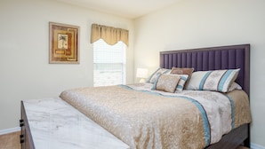A bedroom with a bed, a nightstand, a lamp, and a window with blinds.