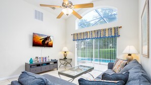 A living room with a sofa, coffee table, TV, and a ceiling fan.