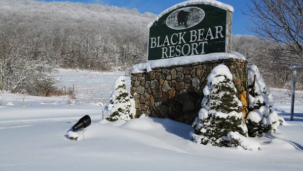 Une enseigne pour le Black Bear Resort, avec une arche en pierre et des arbres couverts de neige en arrière-plan.