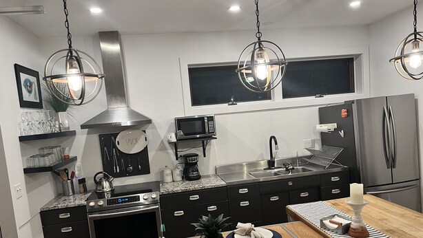 Eine moderne Küche mit schwarzen Schränken, Edelstahlgeräten und einem Holzespeisetisch, gedeckt für zwei Personen.