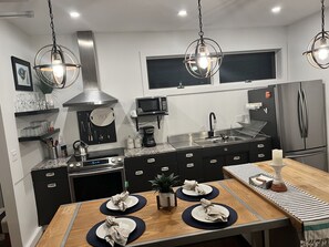 A modern kitchen with a stainless steel refrigerator, a microwave, and a stove. There are two dining tables with placemats and napkins.