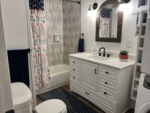 A bathroom with a white vanity, a bathtub, a toilet, and a shower curtain.