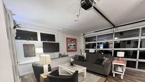 Ein modernes Wohnzimmer mit einem grauen Sofa, schwarzen Sesseln, einem weißen Couchtisch und einem an der Wand befestigten Fernseher.