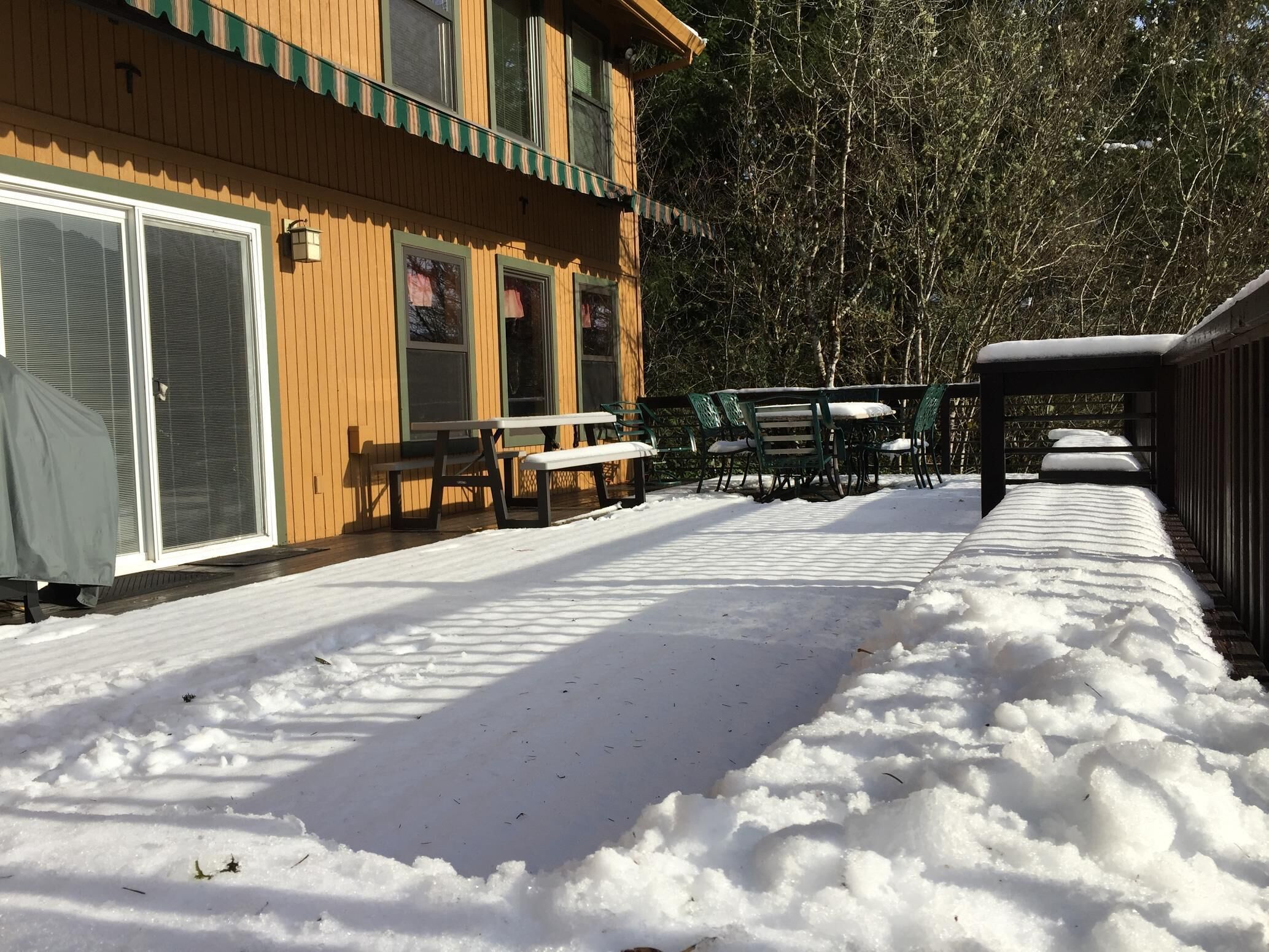 A wooden building with a covered patio area, outdoor seating, and snow on the ground.