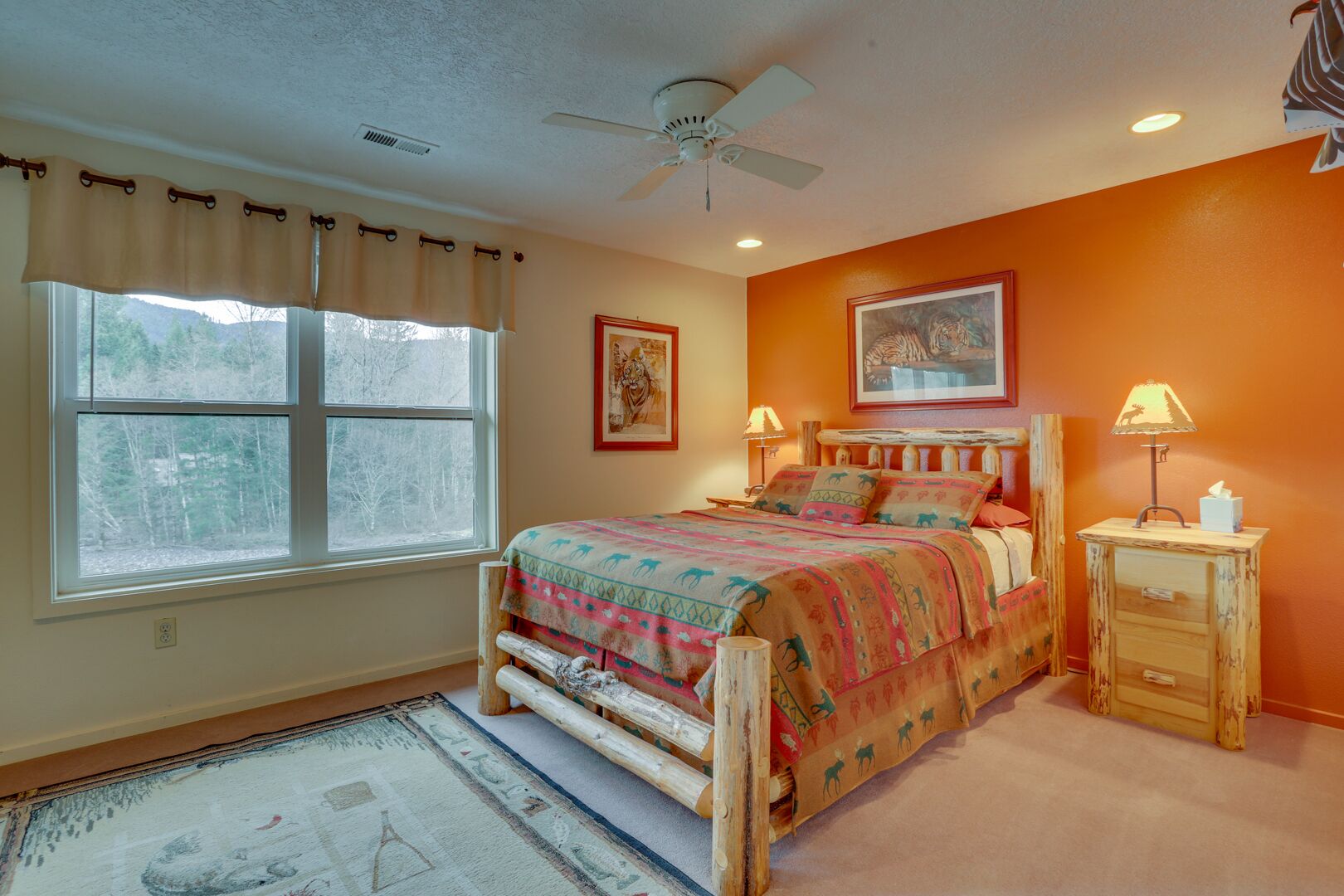 Une chambre à coucher comprenant un lit, deux tables de chevet, un ventilateur de plafond et une fenêtre avec des rideaux.