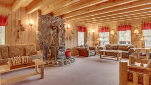 L’intérieur d’un chalet confortable, avec des murs en rondins de bois, une cheminée en pierre, des meubles en bois et de grandes fenêtres ornées de rideaux rouges.