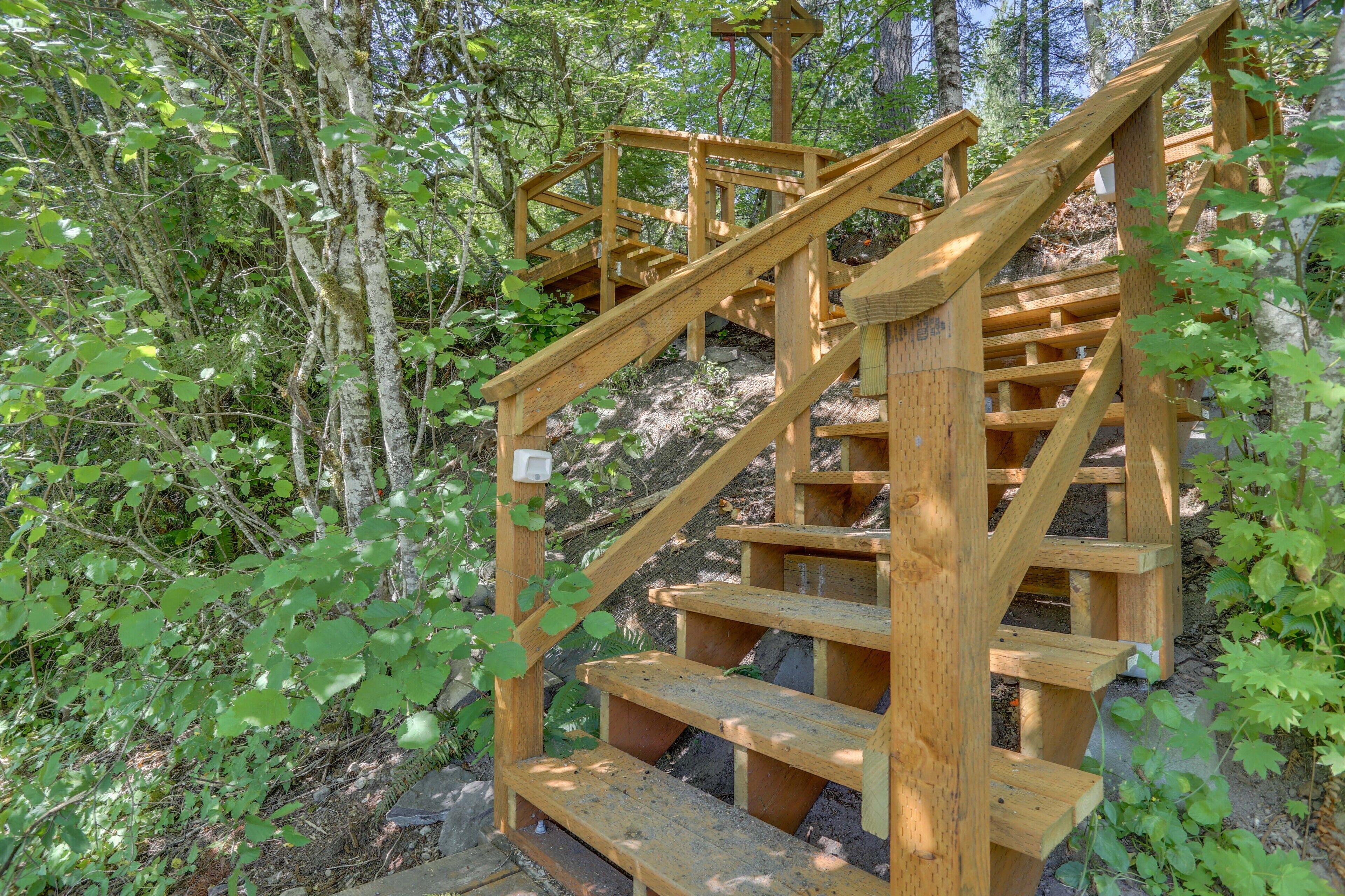 Eine Holztreppe führt einen Hügel hinauf, umgeben von Bäumen und Grün.