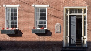 A brick building with two windows, a door with a number plate, and flower boxes on the windowsills. - Family-Friendly 1830s Cville Row House Near Downtown Mall, UVA, & Monticello (Charlottesville)