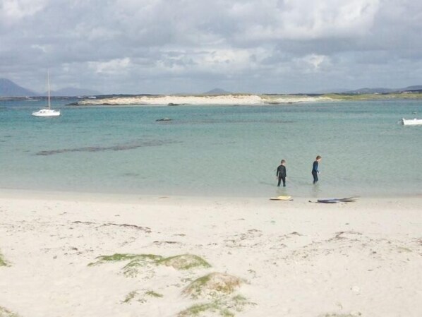 Una playa con agua cristalina, un bote y dos personas de pie en el agua.