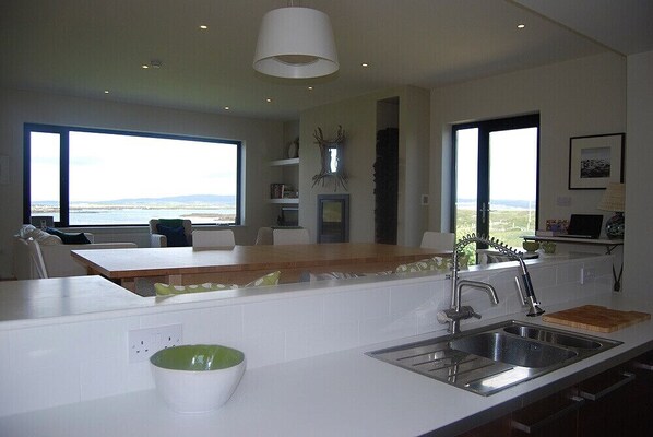 A modern kitchen with a large window, a wooden island, and a view of the ocean. - Ocean Front Home with Spectacular Views Overlooking Mannin Bay (Ballyconneely)