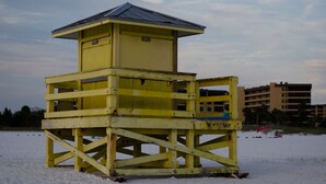 A yellow lifeguard tower with a metal roof, situated on a sandy beach with buildings in the background. - Siesta Key Bungalows: Coquina Bungalows (Sarasota)