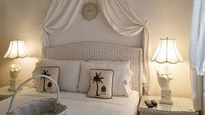 A neatly arranged bedroom with a wicker headboard, white bedding, and decorative pillows with palm tree designs. - Siesta Key Bungalows: Coquina Bungalows (Sarasota)