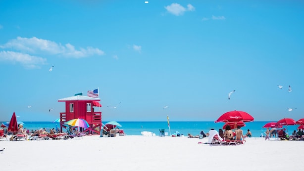 A beach with a lifeguard tower, umbrellas, and beachgoers. - Siesta Key Bungalows: Coquina Bungalows (Sarasota)