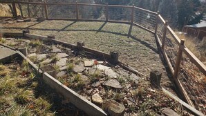 Een omheind buitengebied met een pad van stenen en uitzicht op een bebost landschap.