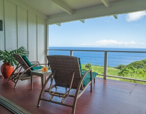 A balcony with wicker chairs and a table, overlooking a coastal view.