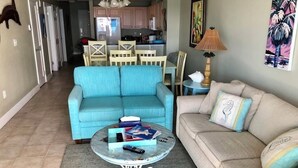 Ein Wohnzimmer mit einem blauen Sofa, einem beigen Sofa und einem Couchtisch mit Büchern und Fernbedienungen.