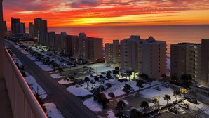 Ein Hochhaus-Hotel mit mehreren Etagen, einem Parkplatz und Blick auf den Sonnenuntergang über dem Meer.