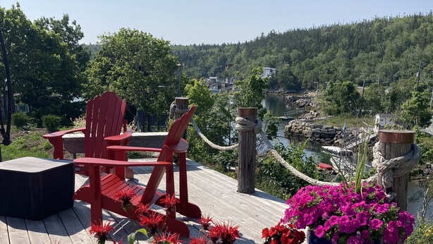 A wooden deck with red Adirondack chairs, a round table, and potted plants with red flowers. - Amazing Unique Church for rent  - St. Cecilia by the Sea (Purcells Cove)