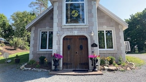 A stone building with a wooden door, large windows, and a clock above the door. - Amazing Unique Church for rent  - St. Cecilia by the Sea (Purcells Cove)