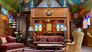 A grand room with a large wooden staircase, a red patterned sofa, a beige armchair, and a red carpet. - Amazing Unique Church for rent  - St. Cecilia by the Sea (Purcells Cove)