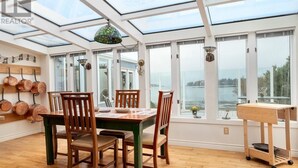 Un comedor con una mesa y sillas, un colgante de luz y vistas a una masa de agua a través de ventanas grandes.