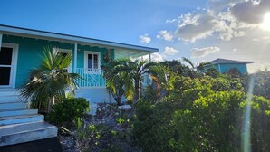 A turquoise house with a porch, surrounded by tropical vegetation.