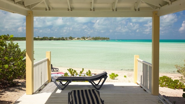 A covered outdoor area with a view of a turquoise sea, two lounge chairs, and a small table.