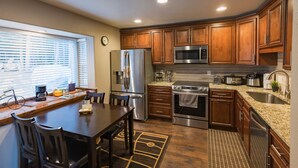 A kitchen with wooden cabinets, stainless steel appliances, a dining table with chairs, and a window with blinds.