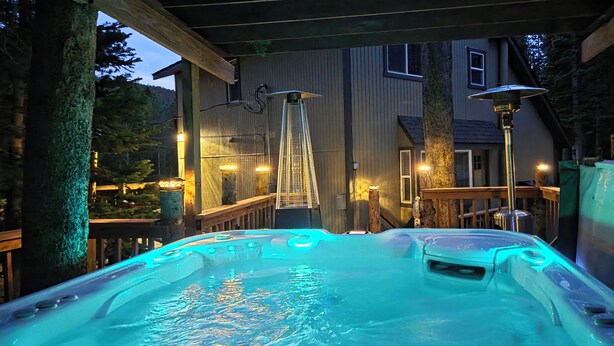 A hot tub area with a wooden deck, a ladder leading to a deck, and a house in the background.