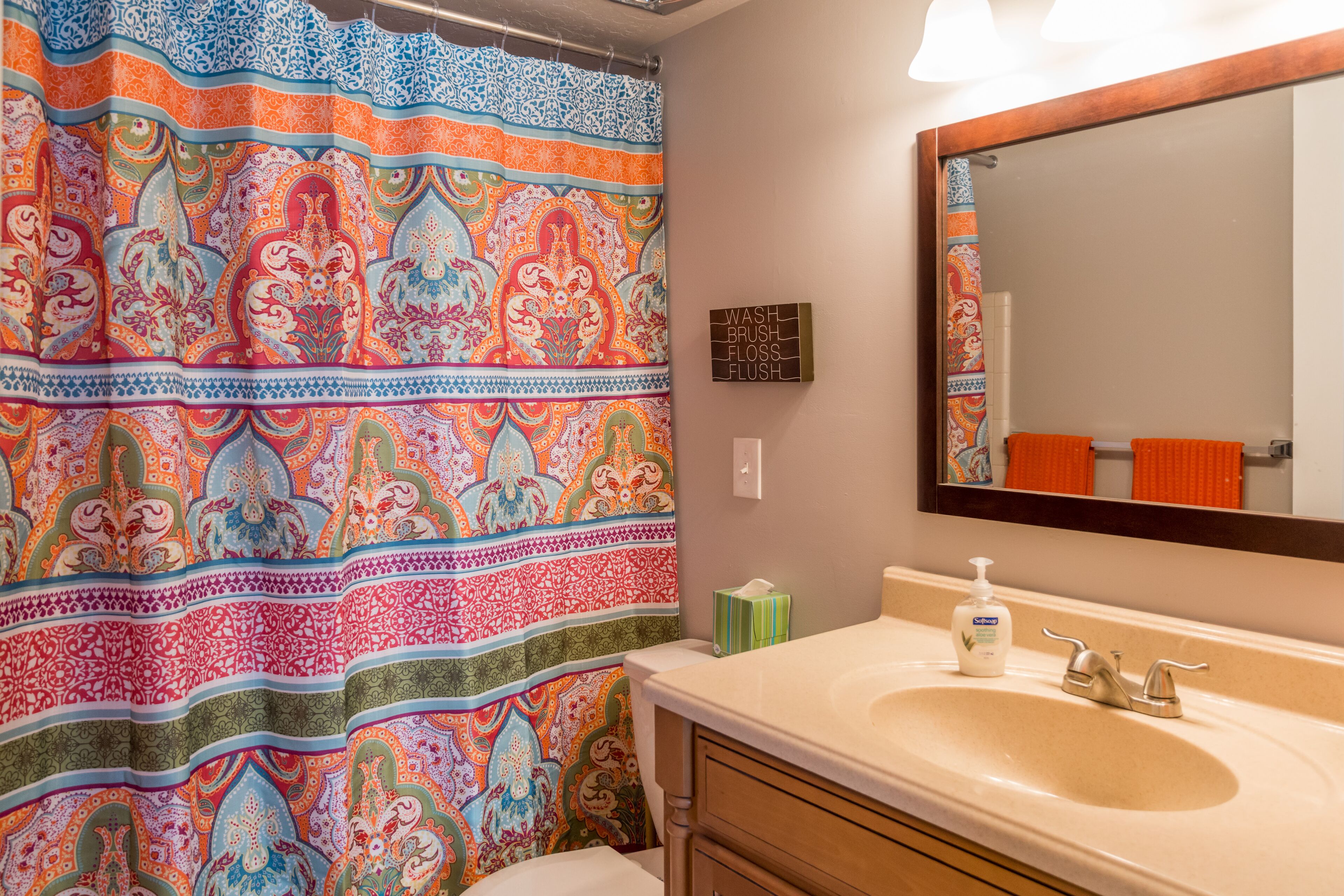 Une salle de bain avec un rideau de douche coloré, un lavabo doté d’un distributeur de savon et un miroir au-dessus du lavabo.