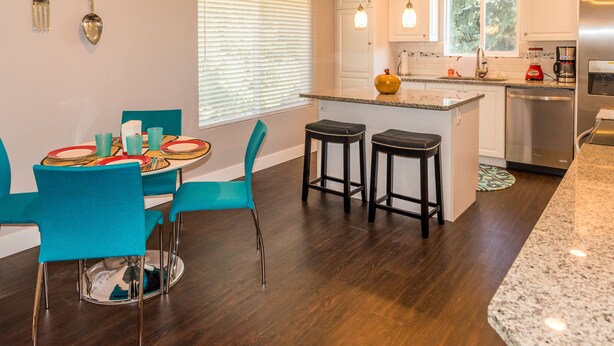 Een moderne keuken met een eethoek, voorzien van een granieten aanrechtblad, roestvrijstalen apparatuur en teal gekleurde stoelen.