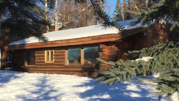 Una baita di legno con il tetto imbiancato dalla neve, circondata da alberi sempreverdi.