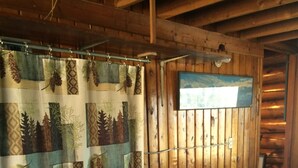Camera da letto di una baita in legno, con un letto coperto da una trapunta decorata con motivi di bosco e animali, una sedia e una finestra che si affaccia sul cielo.