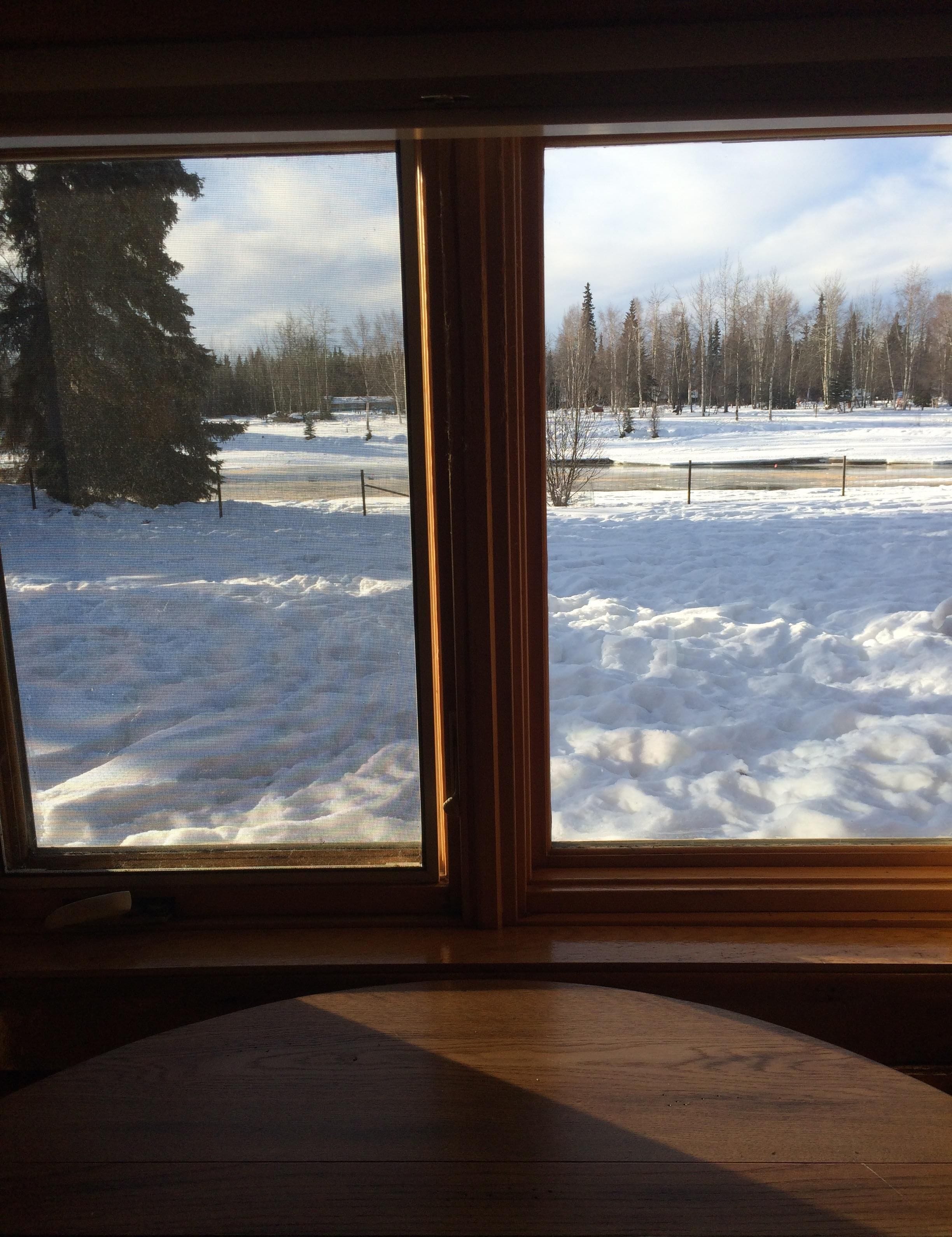 A room with a large window overlooking a snowy landscape with trees and a fence.