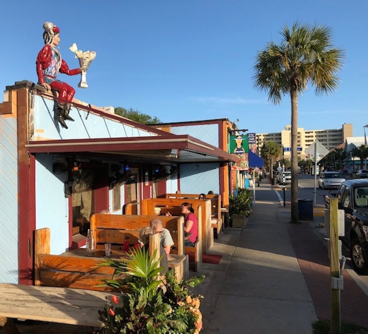 Un ristorante con posti a sedere all'aperto, una palma e una statua sul tetto.