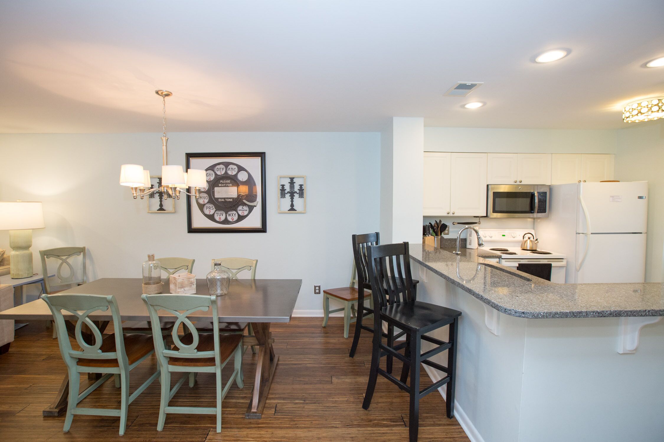 A modern kitchen with white cabinets, a microwave, and a refrigerator. There is a dining area with a table and chairs.