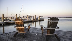 Een houten steiger met twee Adirondack stoelen gericht op een jachthaven met boten.
