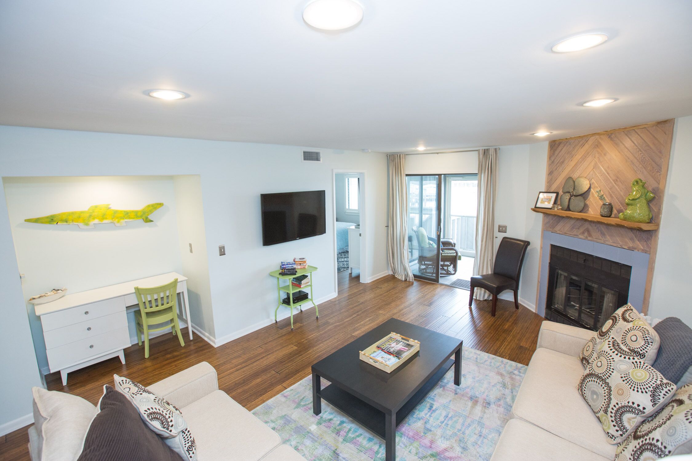 A modern living room with a sofa, coffee table, and a fireplace. There is a TV mounted on the wall and a bookshelf.