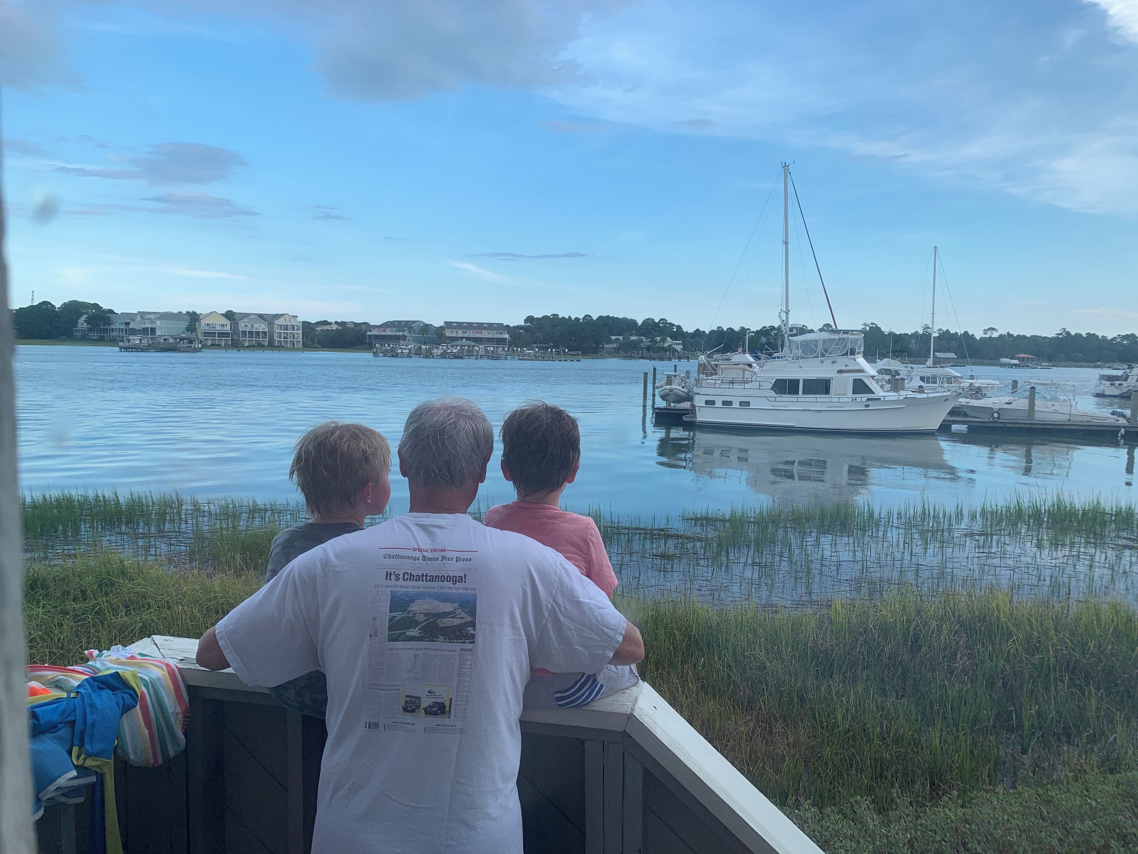 Three people seated on a dock overlooking a marina with boats.