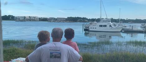 Three people seated on a dock overlooking a marina with boats.