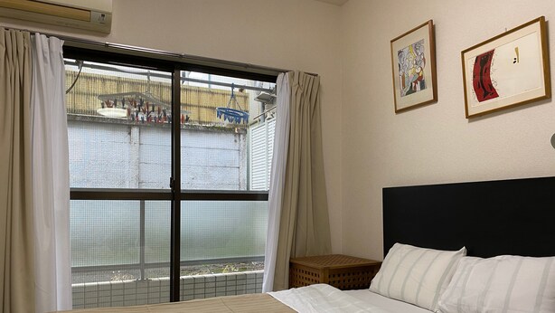 Ein Hotelzimmer mit einem Bett, zwei Handtüchern, einem Kopfteil, einem kleinen Holzhocker und zwei gerahmten Kunstwerken an der Wand.